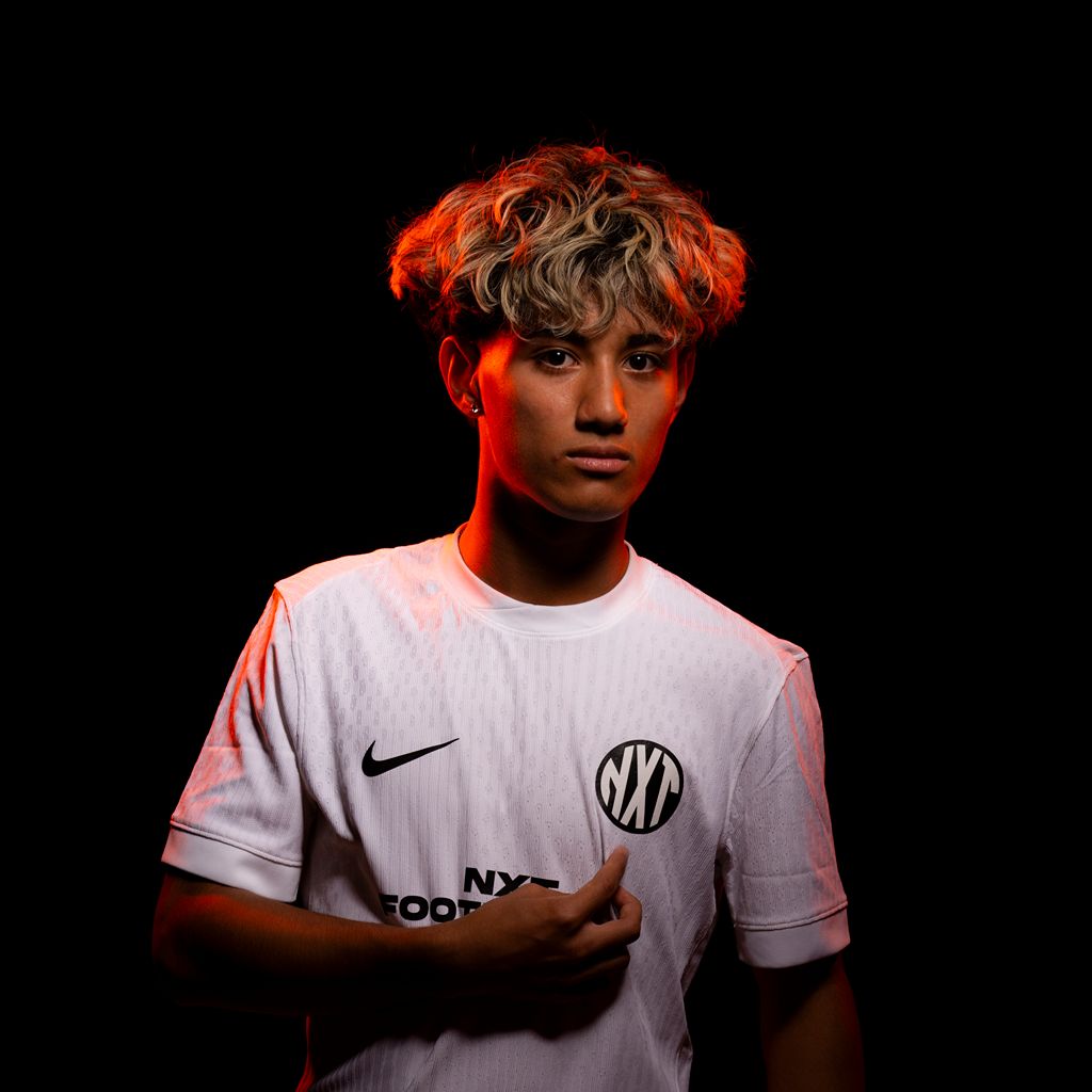 NXT footballer in white uniform pointing at logo